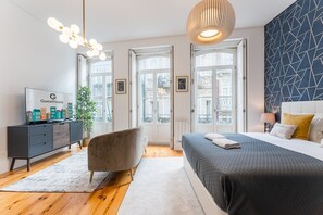 A modern hotel room with a bed, a TV on a dresser, a chair, and a large window. - GuestReady - Amazing Studio in the heart of Porto (Porto)