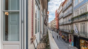 A narrow street with buildings on either side, a balcony with a wooden chair, and a storefront with barrels. - GuestReady - Amazing Studio in the heart of Porto (Porto)