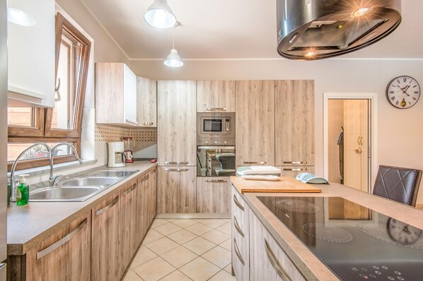 A modern kitchen with wooden cabinets, stainless steel appliances, a built-in oven, and a black induction cooktop.