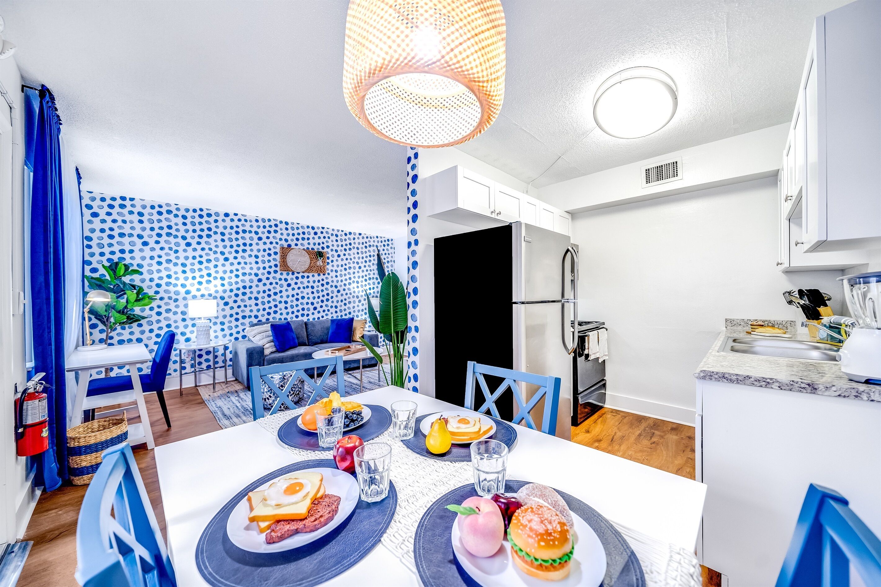 A modern kitchen with white cabinets, a stainless steel refrigerator, and a dining area with a white table set for two.