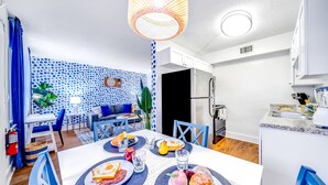 A modern kitchen with white cabinets, a stainless steel refrigerator, and a dining area with a white table set for two. - Water View - King Bed - Palm Wave Says (Coconut Creek)