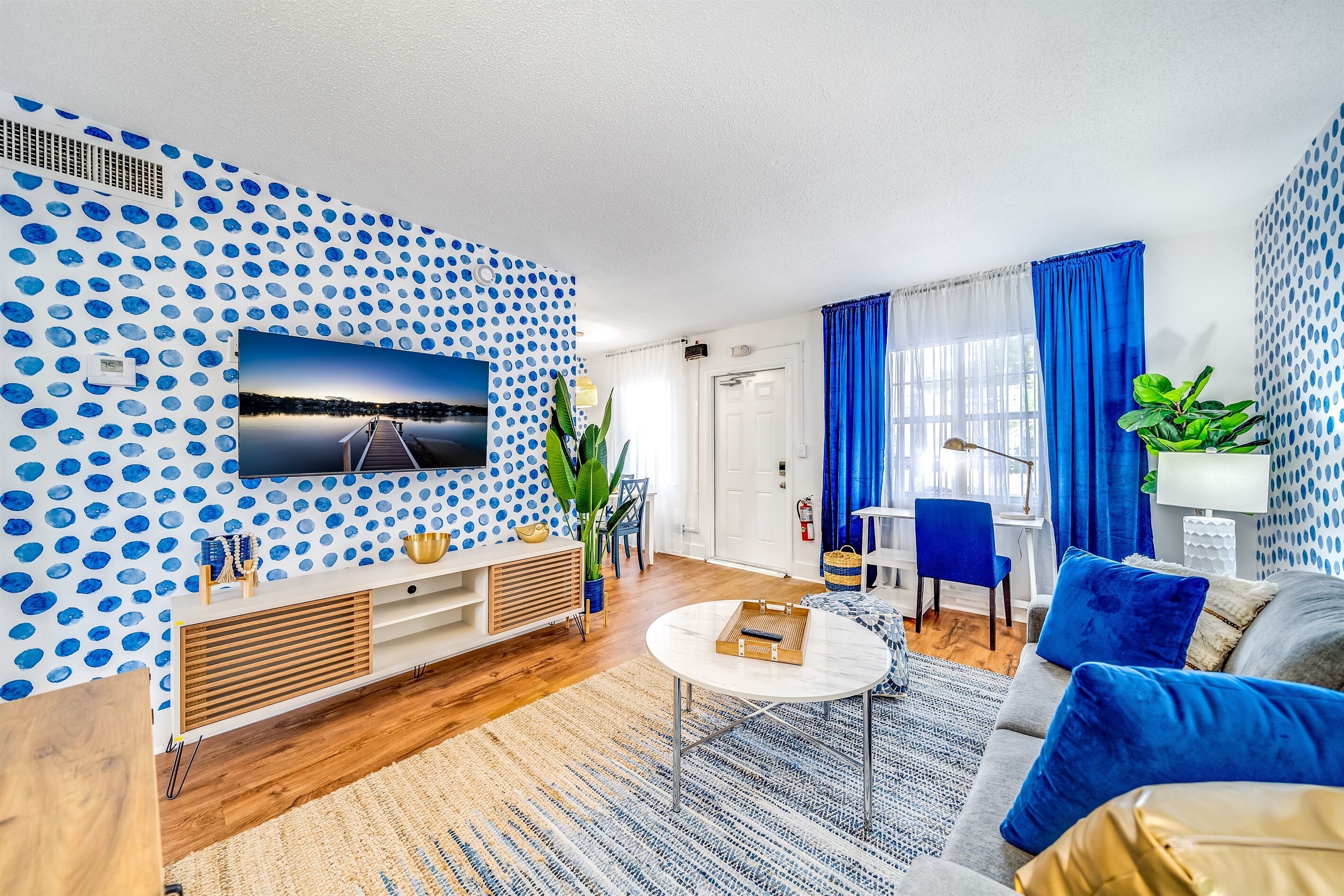 A modern living room with a polka dot wall, a flat-screen TV, a wooden entertainment unit, a round coffee table, and a blue sofa.