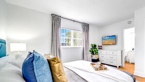 Un dormitorio moderno con cama, mesita de noche y ventana con cortinas.