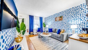 Una sala de estar moderna con papel tapiz azul con lunares, un sofá gris, una mesa de centro y un televisor montado en la pared.