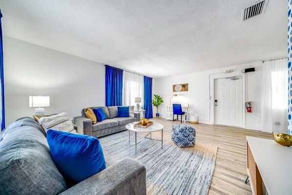 Un salon moderne avec un canapé gris, des coussins bleus, une table basse et un tapis à motifs.