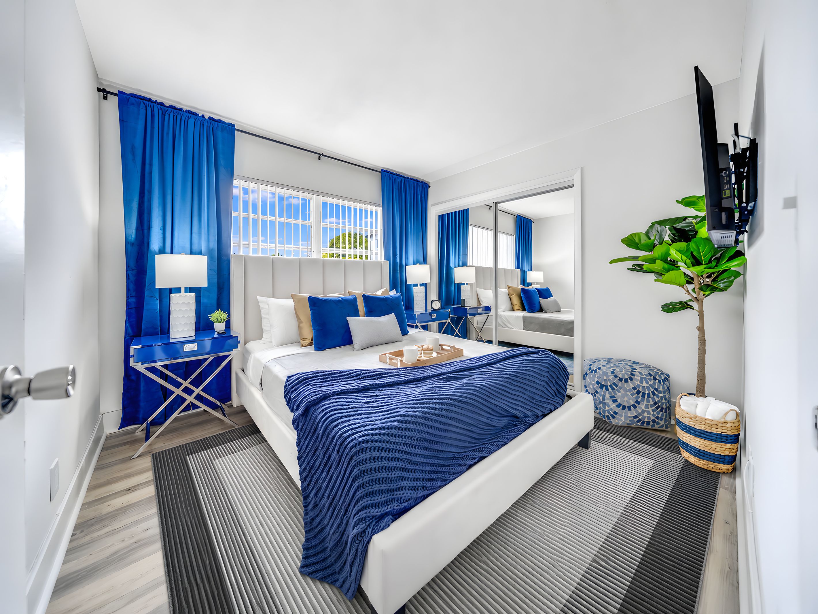 A modern hotel room with a large bed, a desk, a chair, a TV, and a potted plant.