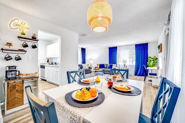 A modern kitchen with white cabinets, a coffee station, and a dining area with blue chairs and a white table set for breakfast.