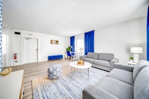 A modern living room with a grey sofa, a blue patterned ottoman, a white coffee table, and a blue sofa. - Water View - Stocked - Palm Wave Says (Coconut Creek)