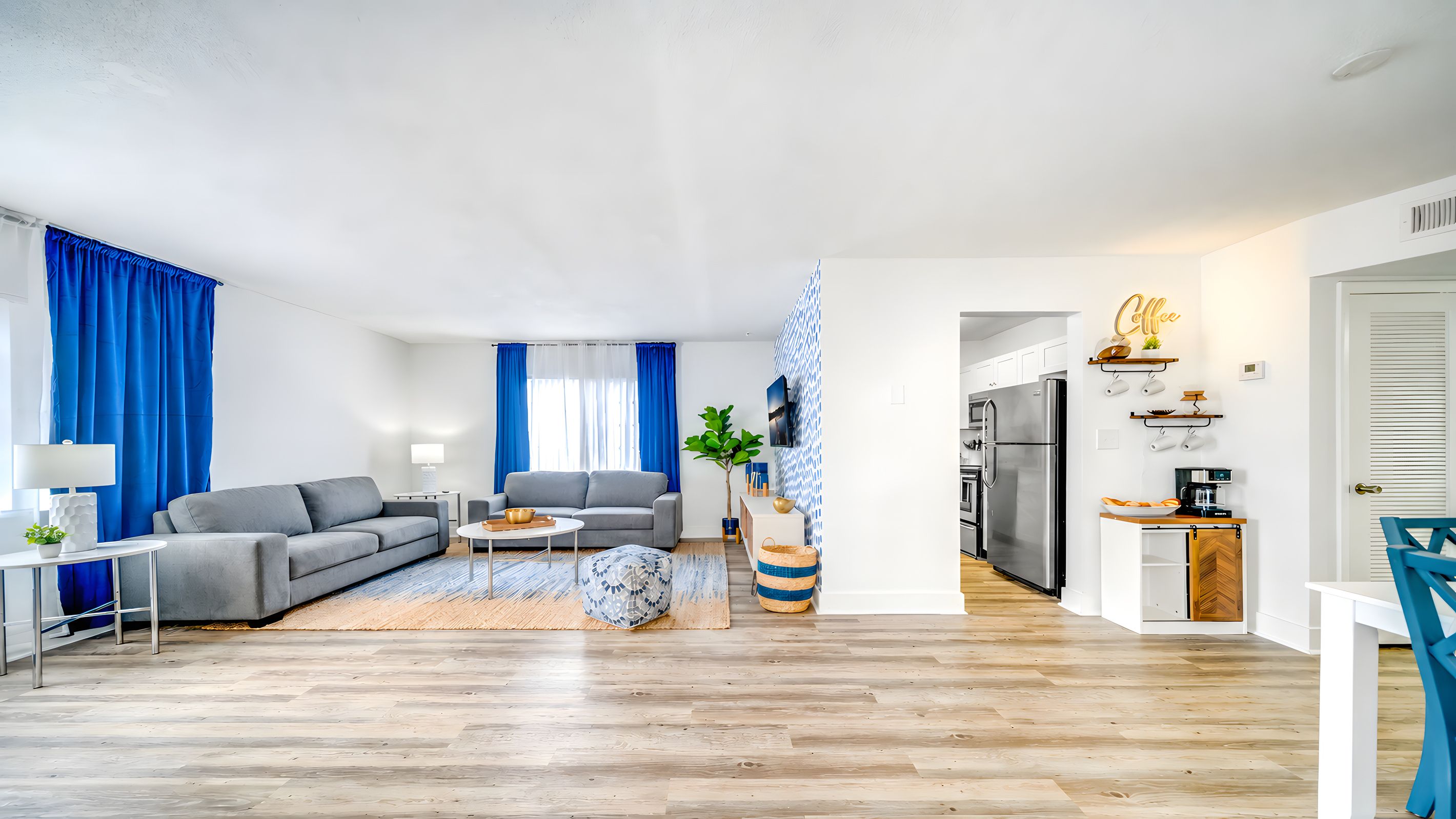 Un salon moderne avec un canapé gris, une table basse et un coin repas agrémenté d’une chaise bleue.