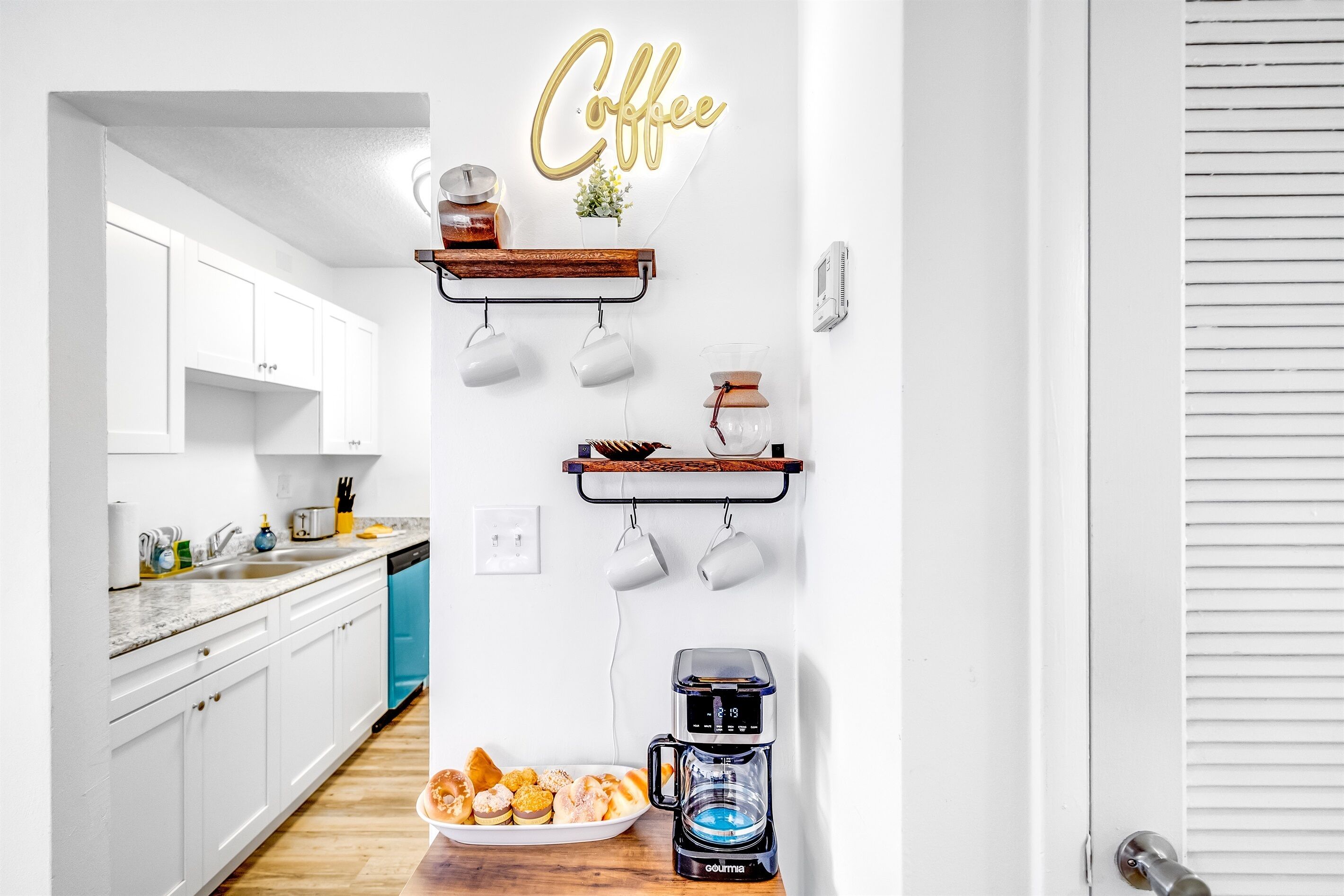 A modern kitchen with white cabinets, a coffee sign, and a coffee maker on the counter.