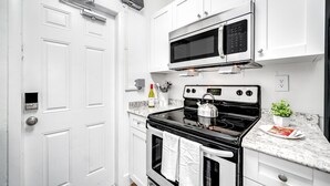 Una cucina moderna con mobili bianchi, un fornello nero, un forno a microonde e una bottiglia di vino sul piano di lavoro.