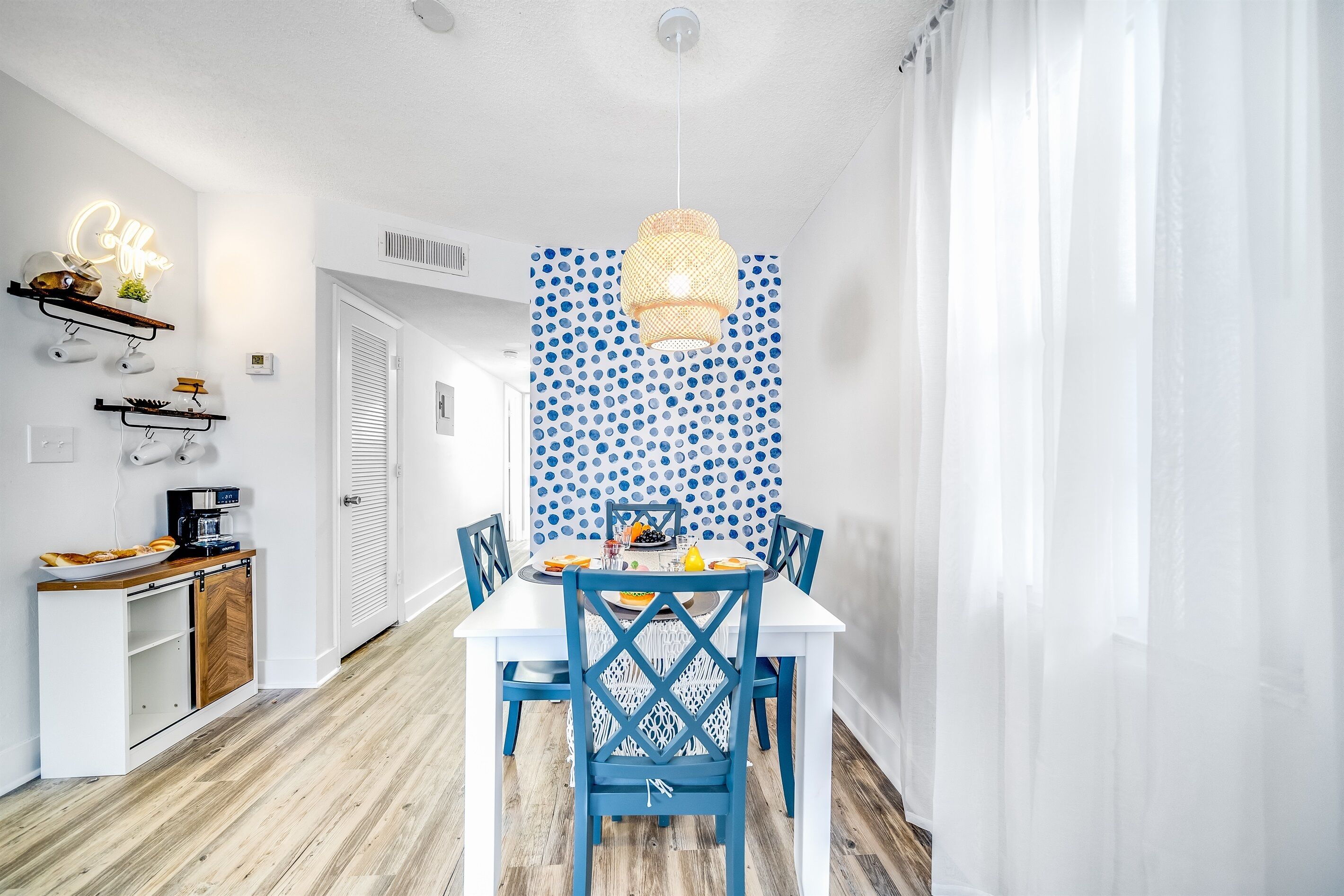 Un coin repas avec une table blanche, des chaises bleues et un mur orné d’un motif.