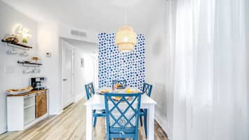 Un coin repas avec une table blanche, des chaises bleues et un mur orné d’un motif.