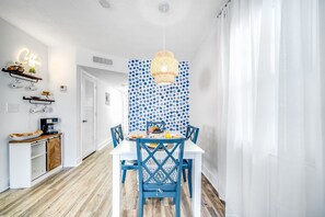 Un coin repas avec une table blanche, des chaises bleues et un mur orné d’un motif.