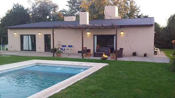 Ett modernt hus med en swimmingpool, utomhusmöbler och en eldstad.