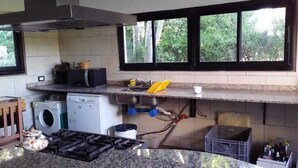 Ett kök med en gasspis, tvättmaskin och ett fönster med utsikt över grönområden.