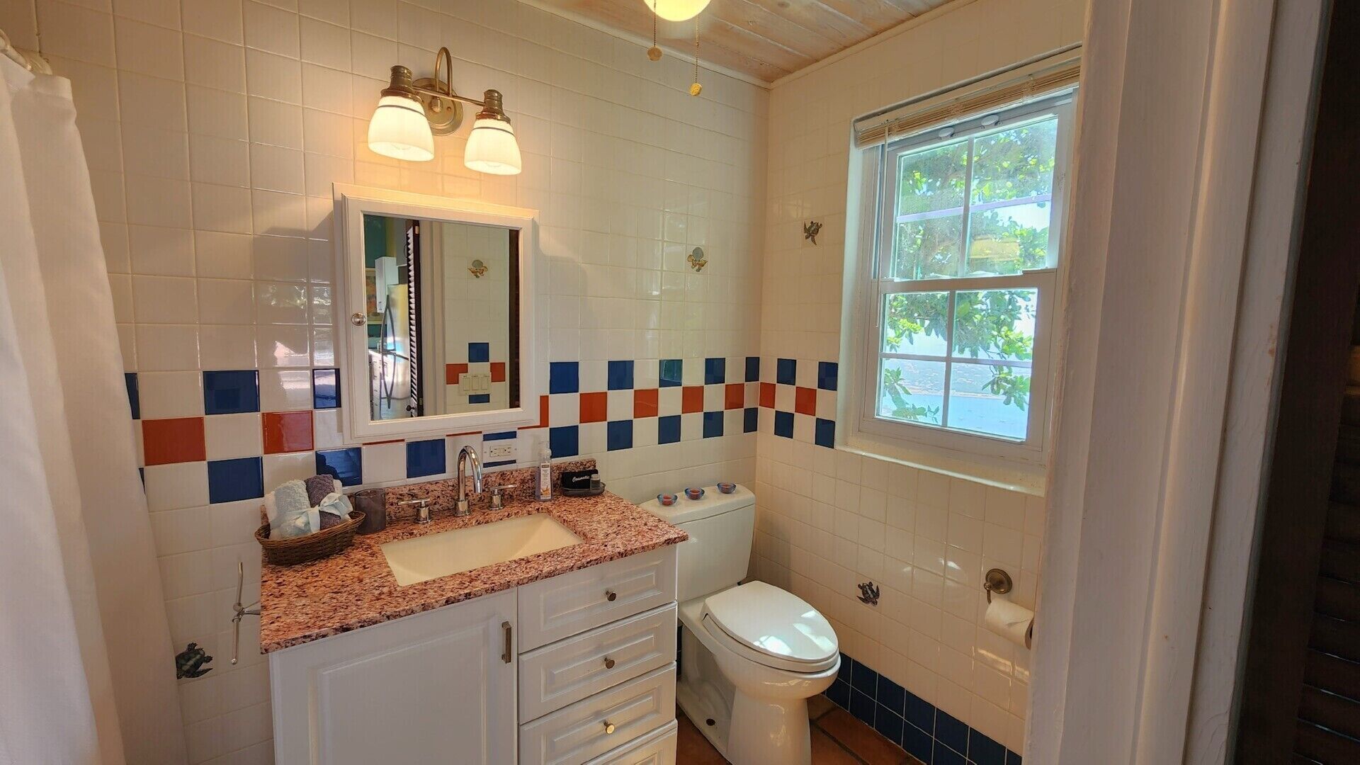 Une salle de bain équipée d’un lavabo, d’un miroir et de toilettes. Une fenêtre offre une vue sur la verdure environnante.