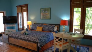 Une chambre à coucher comprenant un lit, une table de chevet, une chaise, un téléviseur et une fenêtre donnant sur un paysage verdoyant.