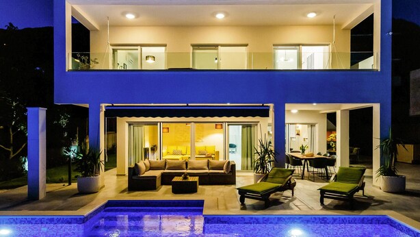 A two-story modern house with a swimming pool, outdoor seating, and a dining area.