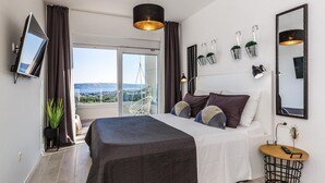 A modern bedroom with a large bed, a TV, a balcony with a view, and a small side table.