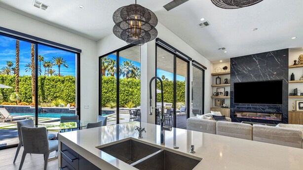 Una cucina moderna con un'isola grande, una TV integrata e vista su piscina e vegetazione.