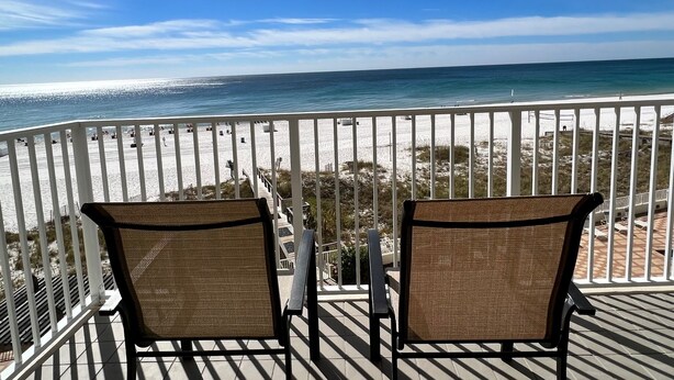 A balcony with two wicker chairs facing a beach.