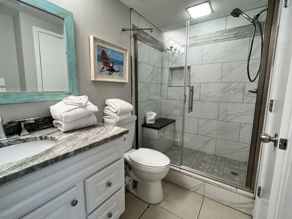 Un baño moderno con tocador de mármol, inodoro, cabina de ducha de vidrio y un cuadro en la pared.