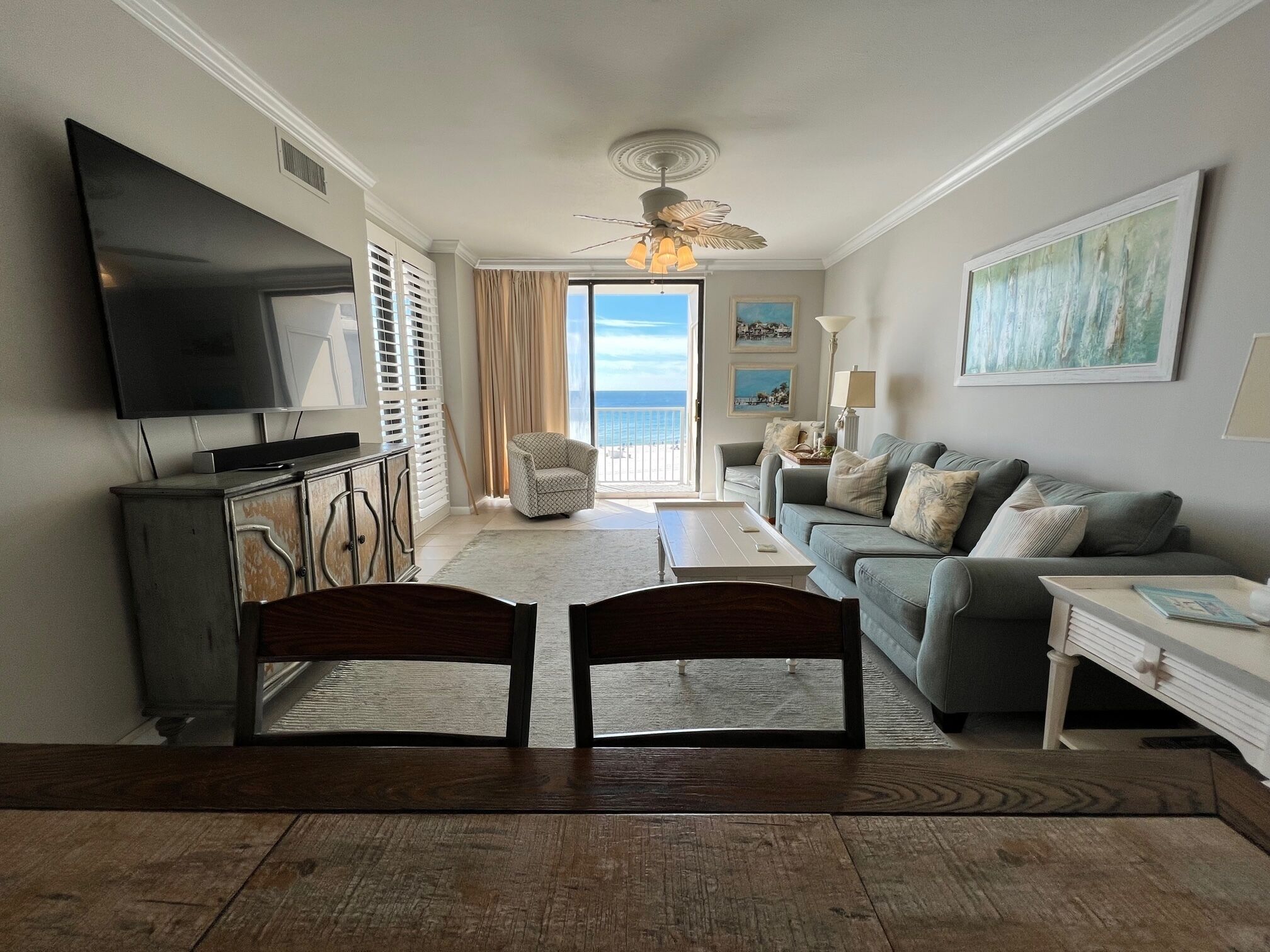 A living room with a television, a sofa, a coffee table, and a view of the ocean.