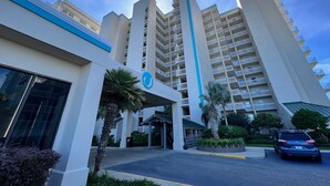 A modern hotel with a prominent blue logo, multiple floors, and a covered entrance area.