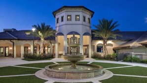 A courtyard with a central fountain, surrounded by palm trees and a building with arched doorways.