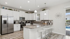 A modern kitchen with white cabinets, stainless steel appliances, a granite countertop, and a bar area with stools.