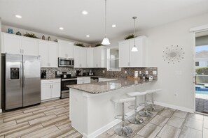 A modern kitchen with white cabinets, stainless steel appliances, a granite countertop, and a bar area with stools.