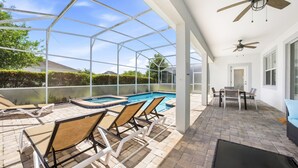 A covered outdoor pool area with lounge chairs, a table, and ceiling fans.