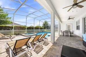 A covered outdoor pool area with lounge chairs, a table, and ceiling fans.