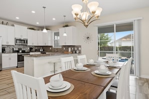 A modern kitchen with white cabinets, a central island, and a dining area with a wooden table and white chairs.