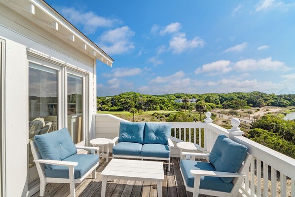 A deck with white furniture and a view of a green landscape.