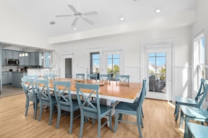 A spacious kitchen with modern appliances, a dining area with a large wooden table and matching chairs, and large windows allowing natural light.
