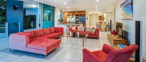 Una sala moderna con un sofá modular rojo grande, una mesa de centro de vidrio y un televisor sobre un mueble de madera.