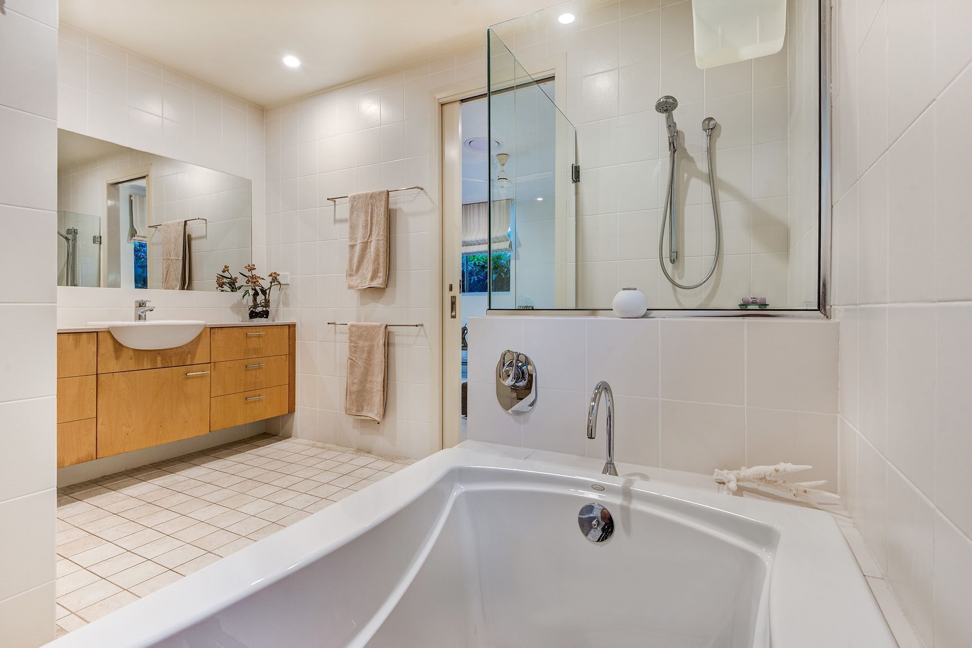 A modern bathroom with a large bathtub, a glass-enclosed shower area, and a wooden vanity with a sink and mirror.