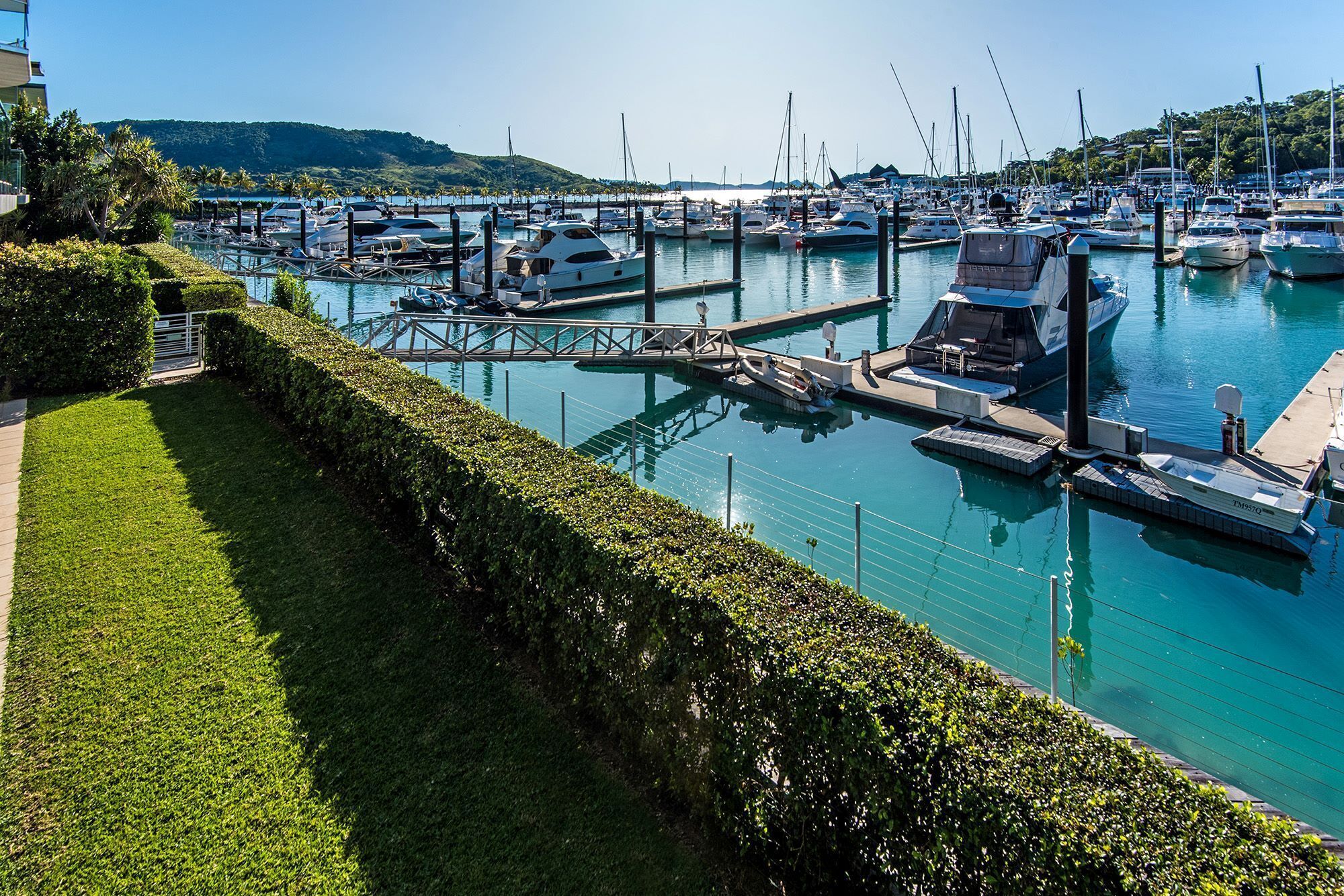 A marina with boats docked at piers, surrounded by well-maintained greenery and a clear sky.