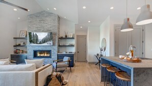 A modern living room with a fireplace, a sofa, a chair, and a dining area with bar stools. - Walk to Gondola: Perfect for Adventures with Private Hot Tub, BBQ & Views! (Park City)