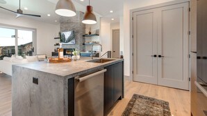 A modern kitchen with a central island, pendant lighting, and a stone accent wall. - Walk to Gondola: Perfect for Adventures with Private Hot Tub, BBQ & Views! (Park City)