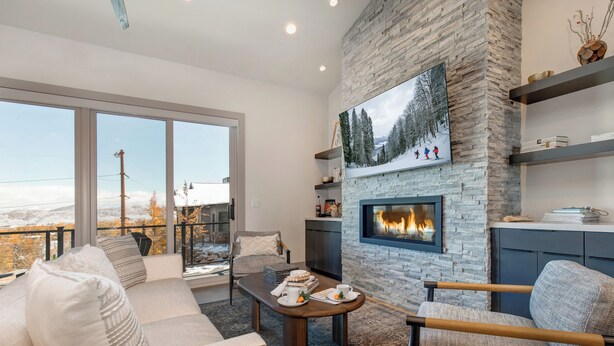 A modern living room with a fireplace, large windows, and a view of the outdoors. - Walk to Gondola: Perfect for Adventures with Private Hot Tub, BBQ & Views! (Park City)