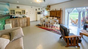 A spacious living area with a sofa, a wooden bench, and a dining table with chairs. There is a kitchen area with cabinets and a refrigerator.