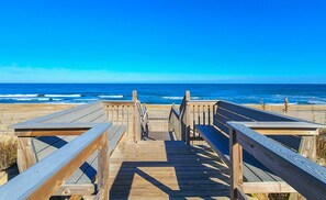 Ein Holzsteg führt zum Strand mit freiem Blick auf das Meer.