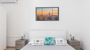 Ein Schlafzimmer mit einem großen Bett, zwei Nachttischen, einem Stadtbild als Gemälde und Blick auf eine Skyline.