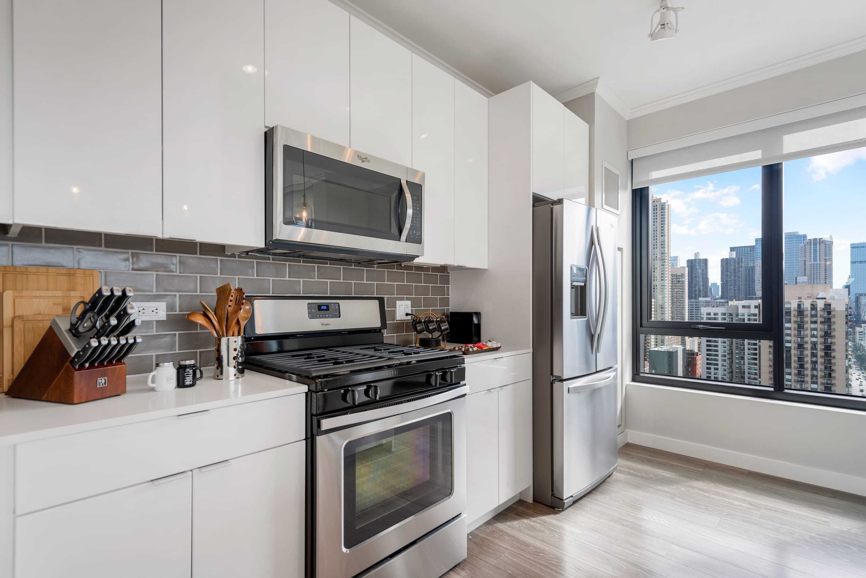 A modern kitchen with white cabinets, a stainless steel stove, a microwave, and a refrigerator.