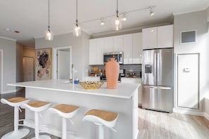 Una cocina moderna con armarios blancos, electrodomésticos de acero inoxidable y una isla central con taburetes de bar.