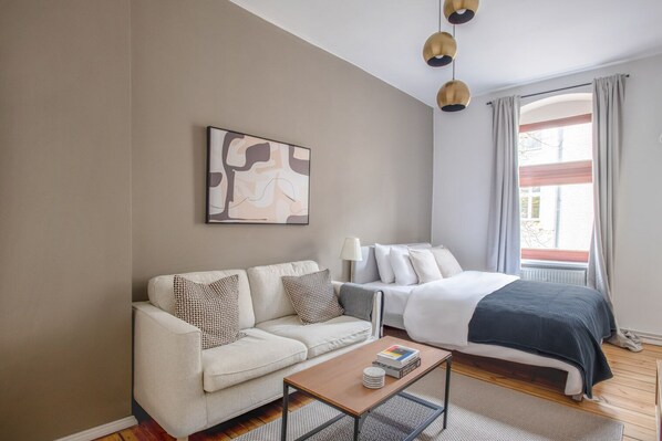 A modern hotel room with a sofa, a bed, a coffee table, and a large window with curtains.