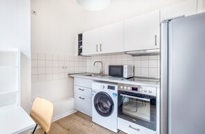 A compact kitchen with white cabinets, a washing machine, an oven, a microwave, and a sink.